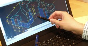 An employee taps at the screen of a desktop computer. A digital blueprint software program is visible on the screen.