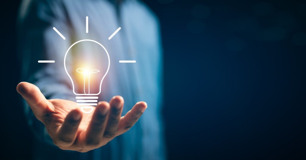 A person wearing a blue shirt holds a glowing light bulb, which symbolizes innovation and new ideas.